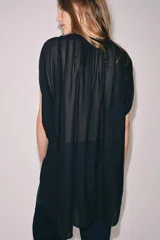 Top estilo túnica color negro confeccionado en punto fino, de manga corta y cuello redondo con frunces. Presenta un diseño holgado con abertura delantera en el bajo.