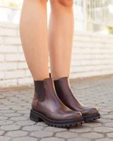 Botas tipo Chelsea de cuero color chocolate, con paneles elásticos laterales, suela track dentada y detalle de textura en el talón.