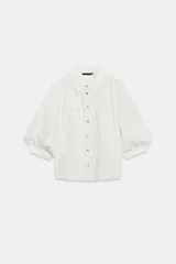 Camisa blanca a rayas sutiles, de cuello solapa y manga abullonada por debajo del codo. Presenta delicados bordados florales perforados en el frente y cierre frontal con botones.