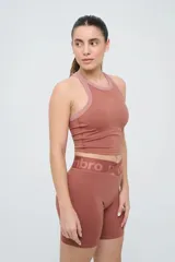 Top deportivo de entrenamiento Umbro modelo Kia, color marrón con detalles en rosa viejo en los ribetes del cuello y sisas. Cuenta con diseño de espalda nadadora y logo de la marca estampado en el pecho.