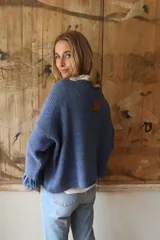 Buzo tejido en punto arroz color azul, con cuello redondo y detalle de flecos en los puños. Presenta un diseño holgado de manga larga y largo hasta la cadera.