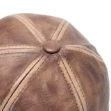 Gorra tipo béisbol confeccionada en cuero sintético color marrón con efecto desgastado y costuras decorativas en contraste.