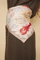 Pañuelo rectangular de seda sintética en tono crudo, con un diseño estampado que incluye ilustraciones coloridas de langostas, aves, sirenas y textos como 'Vini Vidi Amavi'.