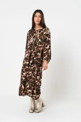 Vestido midi de corte holgado con estampado animal print en tonos marrones y beige. Tiene cuello redondo con lazo, mangas largas abullonadas y falda amplia con volantes. Incluye cinturón marrón con tachas.