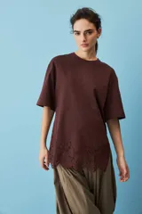 Remera blanca de algodón, de corte oversize, manga corta y cuello redondo, con detalle de aplique de encaje floral en el borde inferior.