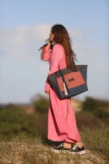 Bolso tipo shopper de gran tamaño, confeccionado en una combinación de lona y gamuza en tonos azul marino, terracota y marrón. Cuenta con doble asa de hombro, cierre superior, bolsillo interior y detalle de borlas decorativas colgantes.