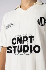 Remera tipo chomba de tejido de punto color blanco, con cuello en V y mangas cortas. Presenta rayas verticales sutiles en la trama y estampado gráfico frontal con la inscripción CNPT STUDIO y detalles en negro.