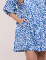 Vestido corto camisero de Elan, con diseño estampado en tonos de azul, cuello camisero clásico, mangas 3/4 abullonadas con elástico en los puños y falda con volantes fruncidos.