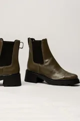 Bota tipo Chelsea de cuero color verde oliva, con paneles laterales elásticos negros y suela track de goma negra con taco cuadrado.