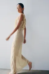 Vestido largo color beige de viscosa, con escote cuadrado, tirantes anchos, detalles drapeados, volantes y aplicaciones de encaje a contraste en el pecho. Cuenta con cierre trasero de botones.