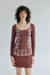 Falda corta de algodón color marrón, con diseño de cinta de seda blanca aplicada en forma de espirales decorativas en el ruedo.