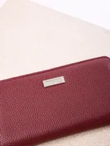 Billetera Rusty modelo Novadi W26, de color bordó con textura granulada, cierre perimetral de cremallera y placa metálica con la marca grabada en el frente.
