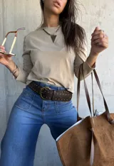 Remera de algodón color beige, de manga larga y cuello redondo, con detalle de tachas metálicas en los hombros.