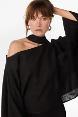 Blusa de lino italiano color negro, con diseño asimétrico de hombro descubierto y cuello tipo choker integrado, de manga larga amplia.