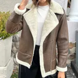 Campera gamulán color marrón con interior de piel sintética color crema, cierre frontal con cremallera descentrada, cuello con solapas amplias y bolsillos laterales.