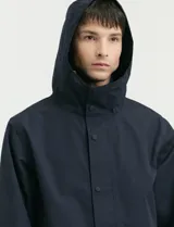 Gabardina con capucha de corte recto y largo medio. Cuenta con cierre frontal engomado, cartera con botones a presión, bolsillos laterales y tejido repelente al agua y al viento.
