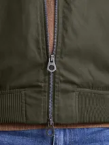 Campera tipo bomber color marrón, confeccionada en tela encerada, con cierre frontal, cuello tipo mao y puños y ruedo acanalados.