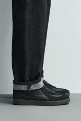 Zapatilla deportiva de estilo retro con diseño de paneles combinados en tonos beige y crema. Presenta detalles en gamuza y una suela de goma en color caramelo.