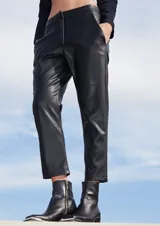 Pantalón sastrero de ecocuero negro, con corte recto, bolsillos delanteros y traseros, y botamanga irregular más corta en la parte frontal.