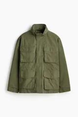 Campera estilo cargo de tejido ripstop, color verde militar, con cuello elevado que incluye capucha oculta. Presenta cierre frontal con solapa rompevientos, cuatro bolsillos delanteros con solapa y botón a presión, puños ajustables y cordón interno en la cintura.
