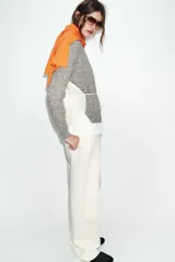 Chaqueta de punto de cuello redondo y manga larga, con diseño combinado que incluye una capa interior en tono crudo. Presenta cierre frontal con botones y puños acanalados.