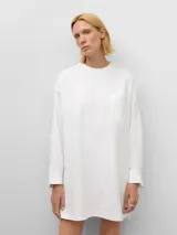 Camisa larga blanca de algodón orgánico, con cuello redondo elástico, manga larga con puño abotonado, bolsillo en el pecho y canesú en la espalda.