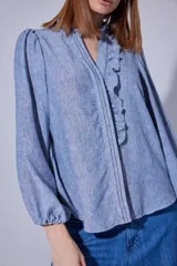 Camisa de manga larga con diseño de rayas verticales sutiles, cuello camisero con volados frontales y mangas abullonadas con puños ajustados.