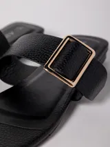 Sandalia baja negra de cuero sintético, con tira ancha sobre el empeine con hebilla metálica dorada y tira para el dedo.