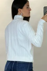 Buzo de hilo de punto con diseño de trenzas verticales, cuello alto y cadena metálica decorativa incorporada en la parte frontal.