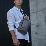 Riñonera bandolera de diseño ergonómico en color gris, con cierres waterproof y correa ajustable. Cuenta con tres divisiones internas y puede llevarse cruzada al frente o en la espalda.
