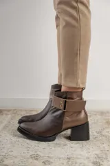 Bota corta de cuero negro con acabado combinado mate y charol. Presenta una tira decorativa con tachas metálicas y hebilla en el tobillo, tacón cuadrado robusto y suela con plataforma.