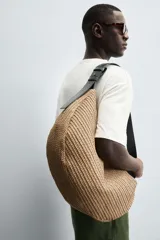 Bolso de hombro negro con acabado trenzado. Tiene un compartimento principal con cierre de cremallera y un bolsillo plano en el interior. El asa de hombro es ajustable.