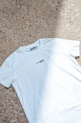 Remera blanca de manga corta con cuello redondo, pequeña estampa frontal y etiqueta decorativa en el borde inferior.