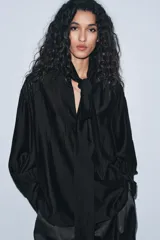 Camisa fluida de cuello redondo con escote en pico y lazada frontal en el mismo tejido. Presenta mangas largas con puños anchos y bajo recto.