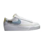 Championes Nike Blazer Low Platform Next Nature, de diseño bajo con plataforma. Presentan un cuerpo de lona blanca con detalles en cuero texturizado, un swoosh lateral en color celeste y un pequeño parche bordado decorativo. Incluyen refuerzos en la puntera y el talón en tonos neutros.