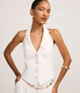 Chaleco sastre de frente única, color blanco, con cuello solapa, cierre frontal con botones y ruedo en punta en forma de V. Presenta un diseño entallado y espalda descubierta.