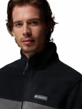 Campera polar de Columbia con cierre frontal completo, cuello alto y diseño de bloques de color en negro y gris. Cuenta con bolsillos laterales con cierre y logo de la marca bordado en el pecho.