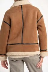 Campera tipo gamulán de corte oversize, confeccionada en material efecto gamuza color camel con interior y detalles de cuello y puños en corderito sintético color crema. Presenta cierre frontal y detalles de ribetes en cuero sintético negro.