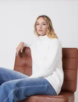 Polera de punto grueso color blanco, con cuello alto, mangas largas de corte ranglan y diseño de texturas combinadas.