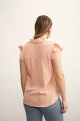 Camisa color amarillo pálido con textura arrugada, cuello mao con volados, cierre frontal con botones y mangas cortas con volados.