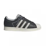 Championes adidas Superstar de diseño clásico con exterior de cuero sintético en color gris oscuro, icónica puntera de goma y suela de plataforma en tono crema. Presenta las tres bandas laterales en un tono gris más claro y el nombre del modelo en letras plateadas.