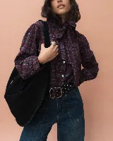 Bolso tipo hobo de gran tamaño, confeccionado en gamuza color marrón oscuro. Presenta un diseño artesanal con costuras visibles y detalles de tientos en el cuerpo, asa integrada con pespuntes a mano y cierre superior.