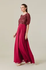 Vestido largo de fiesta color bordó, con cuerpo superior bordado en lentejuelas al tono, mangas cortas tipo capa y falda fluida de corte evasé con cintura definida.