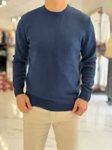 Buzo de hilo color beige claro, con cuello redondo y diseño clásico de manga larga.