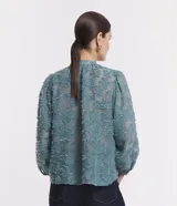 Camisa celeste en tejido chiffon con textura de bordado con felpas, cuello mao, abotonadura frontal y mangas largas abullonadas.