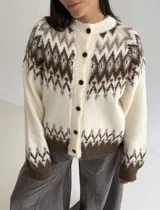 Cardigan de punto con diseño jacquard de inspiración nórdica, en tonos blanco, gris y marrón. Presenta cuello redondo, cierre frontal con botones y mangas largas con puños acanalados.