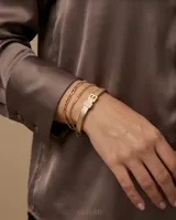 Esclava rígida de acero con baño de oro, con textura grabada y detalle de hebilla decorativa con incrustaciones de circonias.