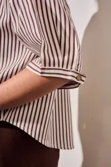 Camisa de corte oversize con estampado de rayas verticales en tonos marrón y beige. Presenta cuello camisero, cierre frontal con botones y mangas cortas con caída relajada.