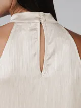 Blusa color crema de poliéster con textura plisada, cuello alto y corte sin mangas. Presenta cierre de botón y ojo de cerradura en la parte posterior del cuello y bajo con acabado ondulado.