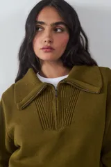 Sweater de punto color verde oliva, con cuello polo y cierre frontal parcial, de manga larga con puños anchos y diseño acanalado en el bajo.